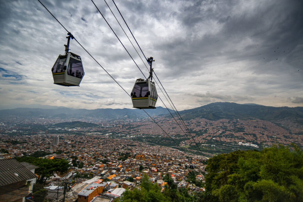 Medellin city in Colombia with endless spread of buildings as seen from a mountain with cable (funicular) cars above and dramatic cloudy sky in the back